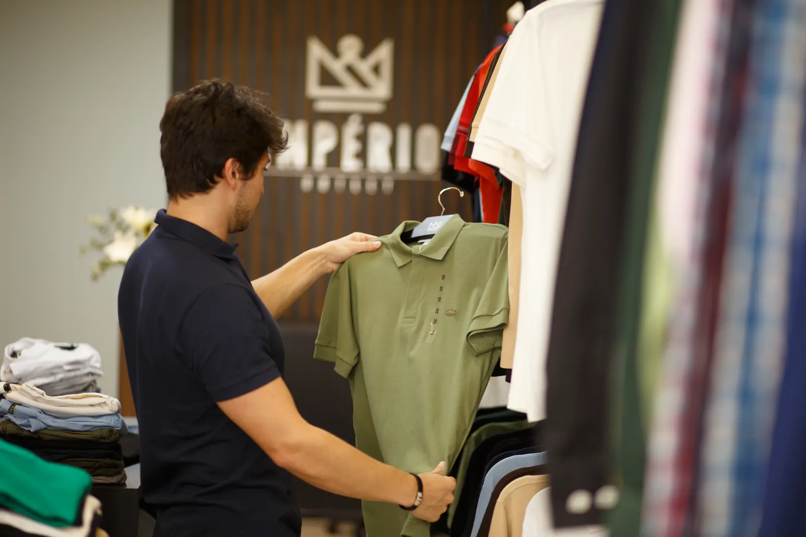 Cliente ajustando uma camisa polo verde dentro da loja Império Outlet